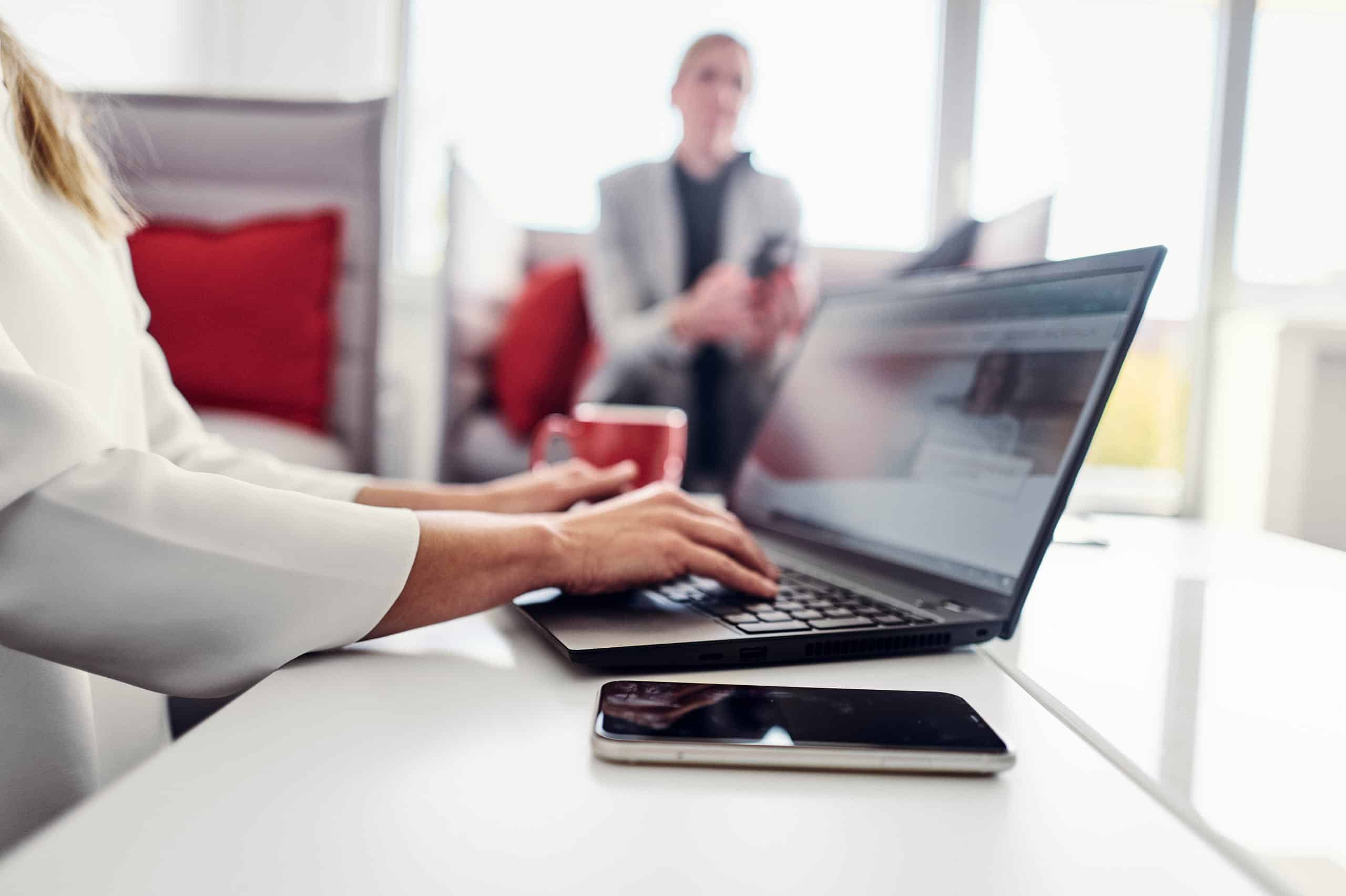 Osoba siedzi na sofie w salonie kwsoft i przegląda stronę internetową Kwsoft na swoim laptopie.