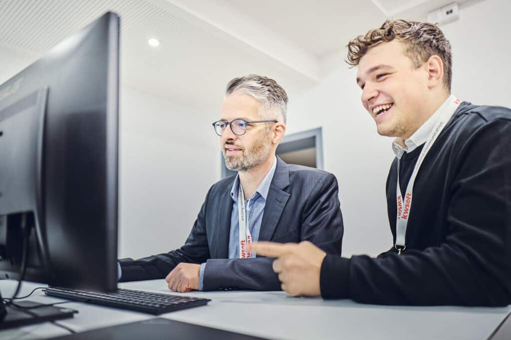 Julius Binninger and Markus Singer are sitting in front of a screen and looking at it.