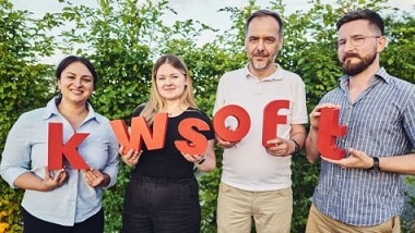 Two women and two men are holding red letters that spell kwsoft